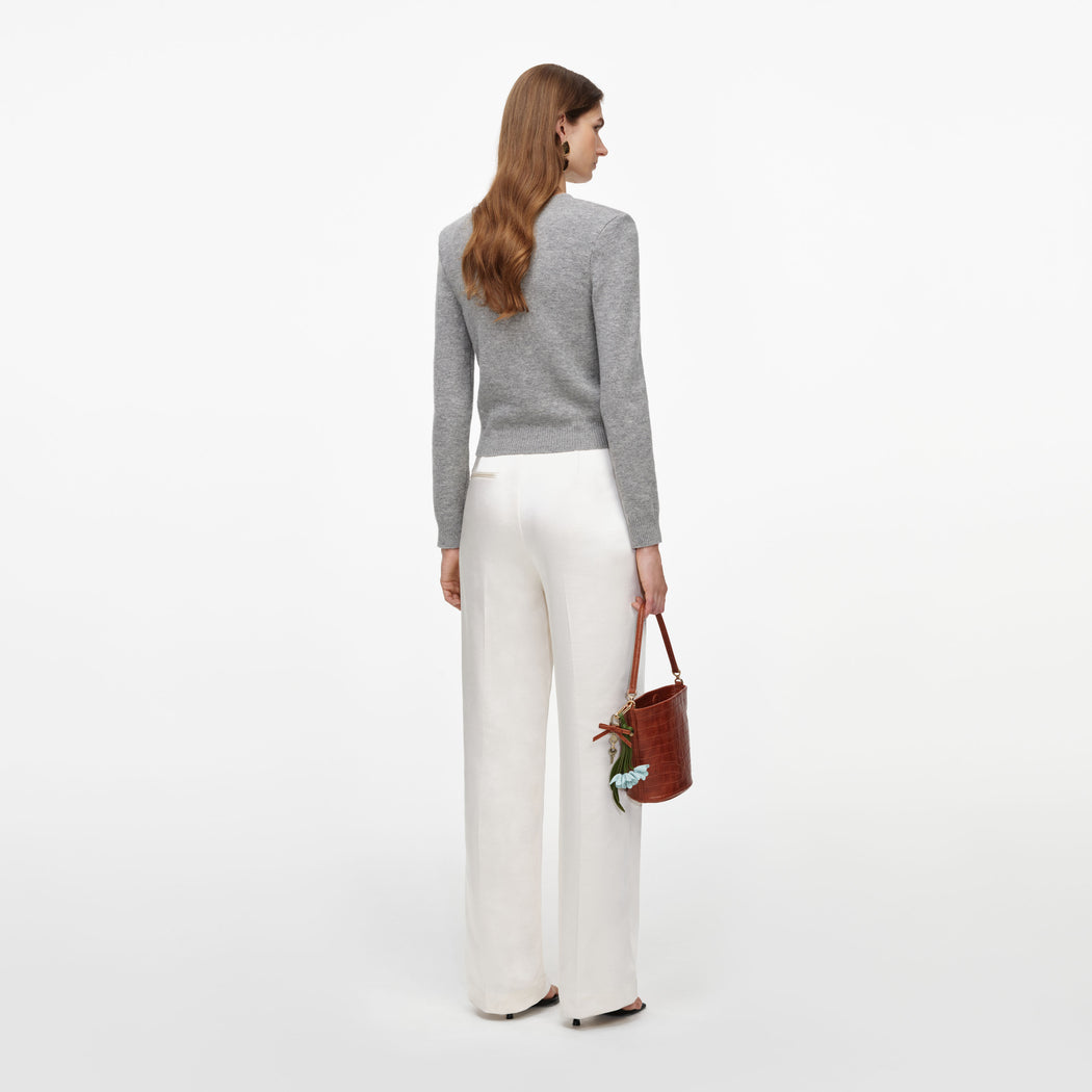 Woman facing away wearing a grey long-sleeved top, white wide-leg trousers, and holding a brown handbag