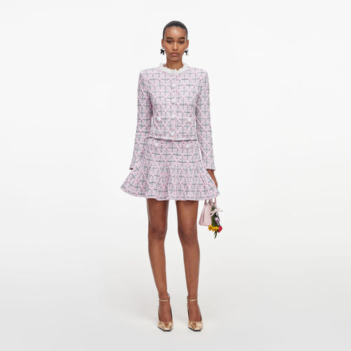 Woman in pink tweed jacket and matching skirt, holding a small pink handbag with flower charms