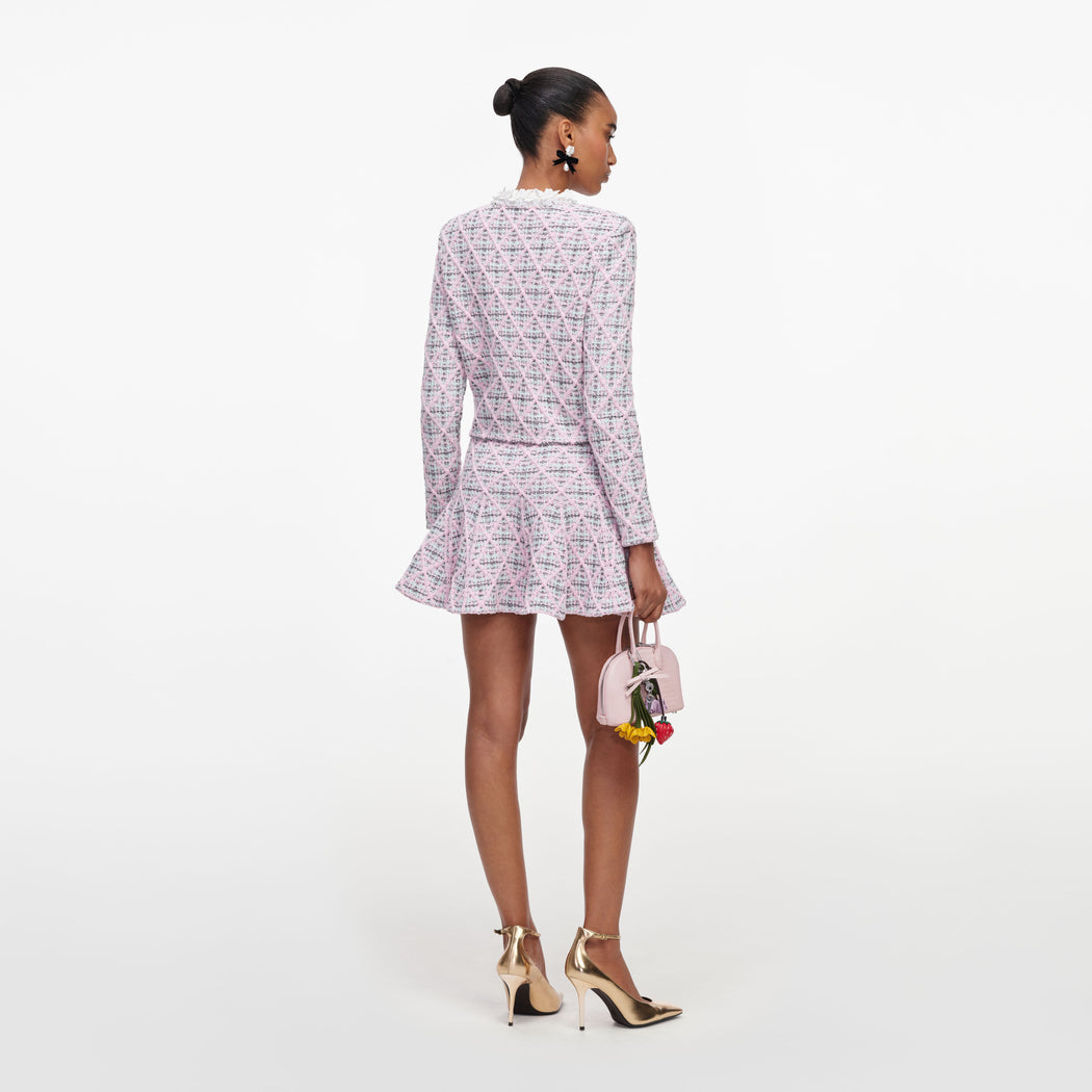 Model from behind wearing a pink tweed jacket and matching skirt, holding a small pink handbag