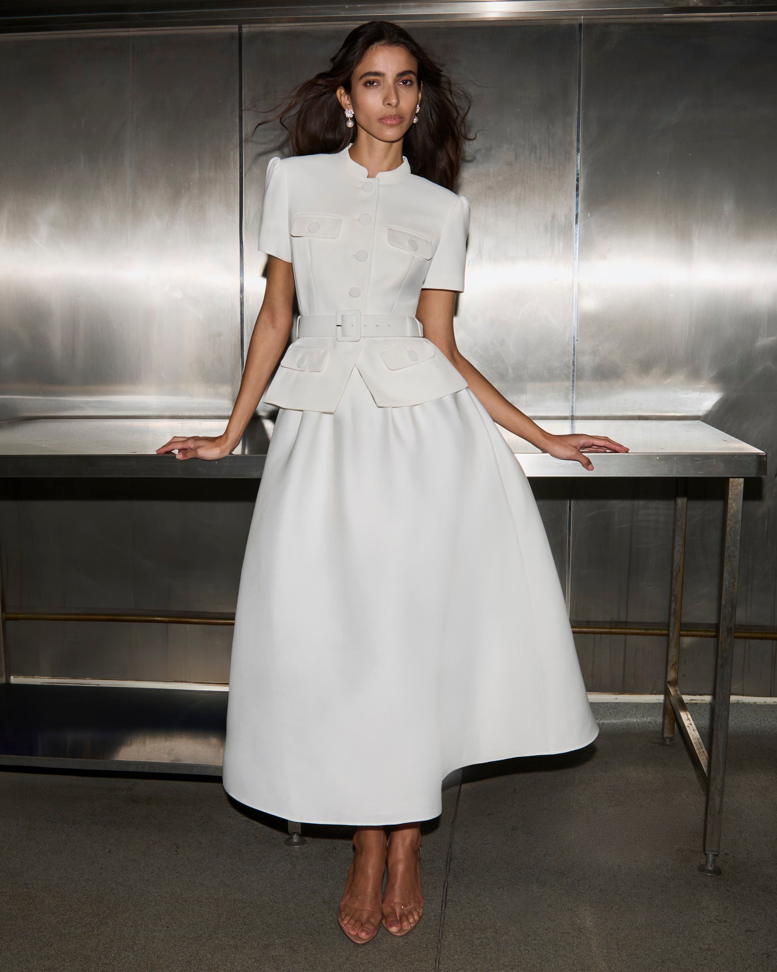 Woman in a white dress standing in front of a metallic wall.