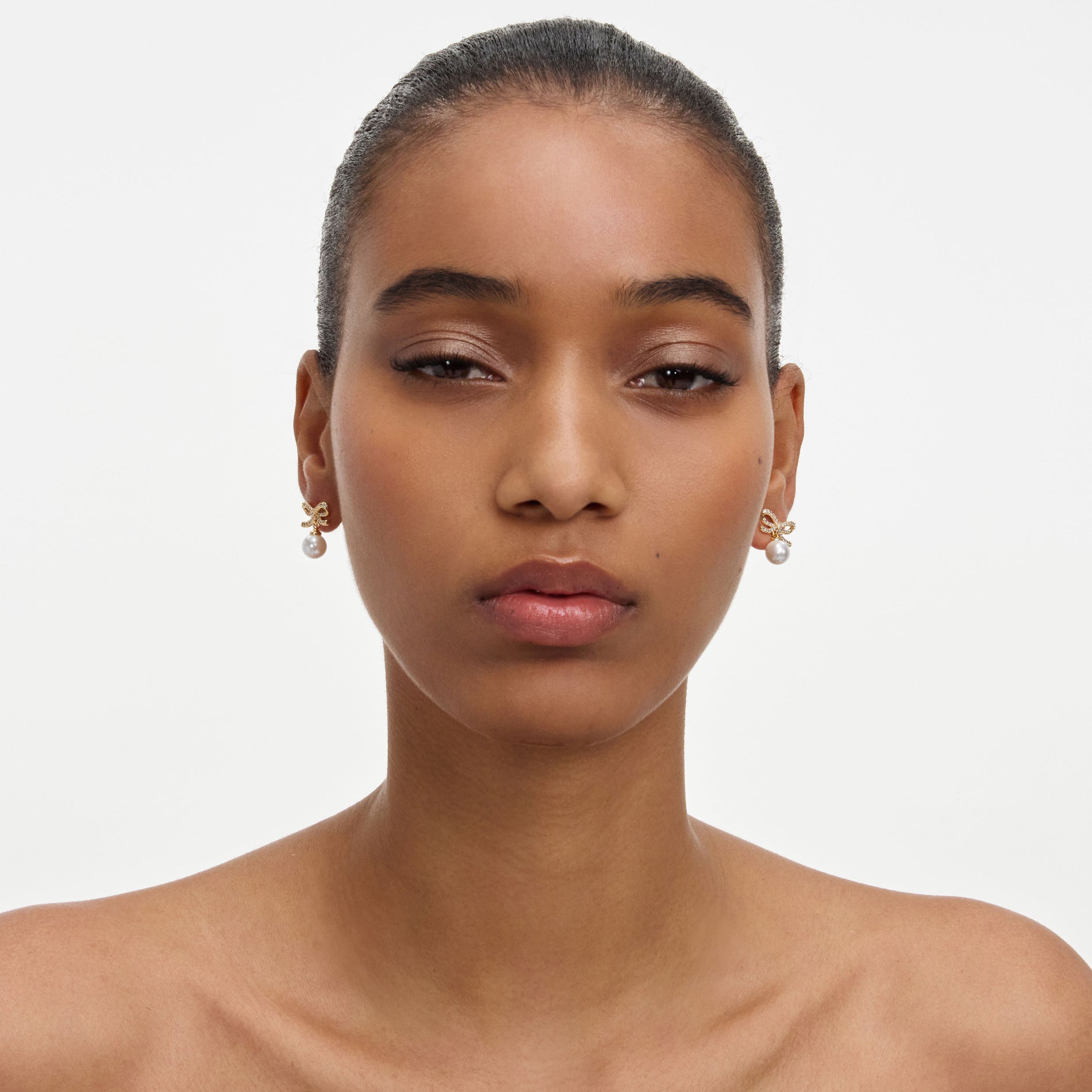 A close up of a woman wearing the Gold Bow Pearl Earrings