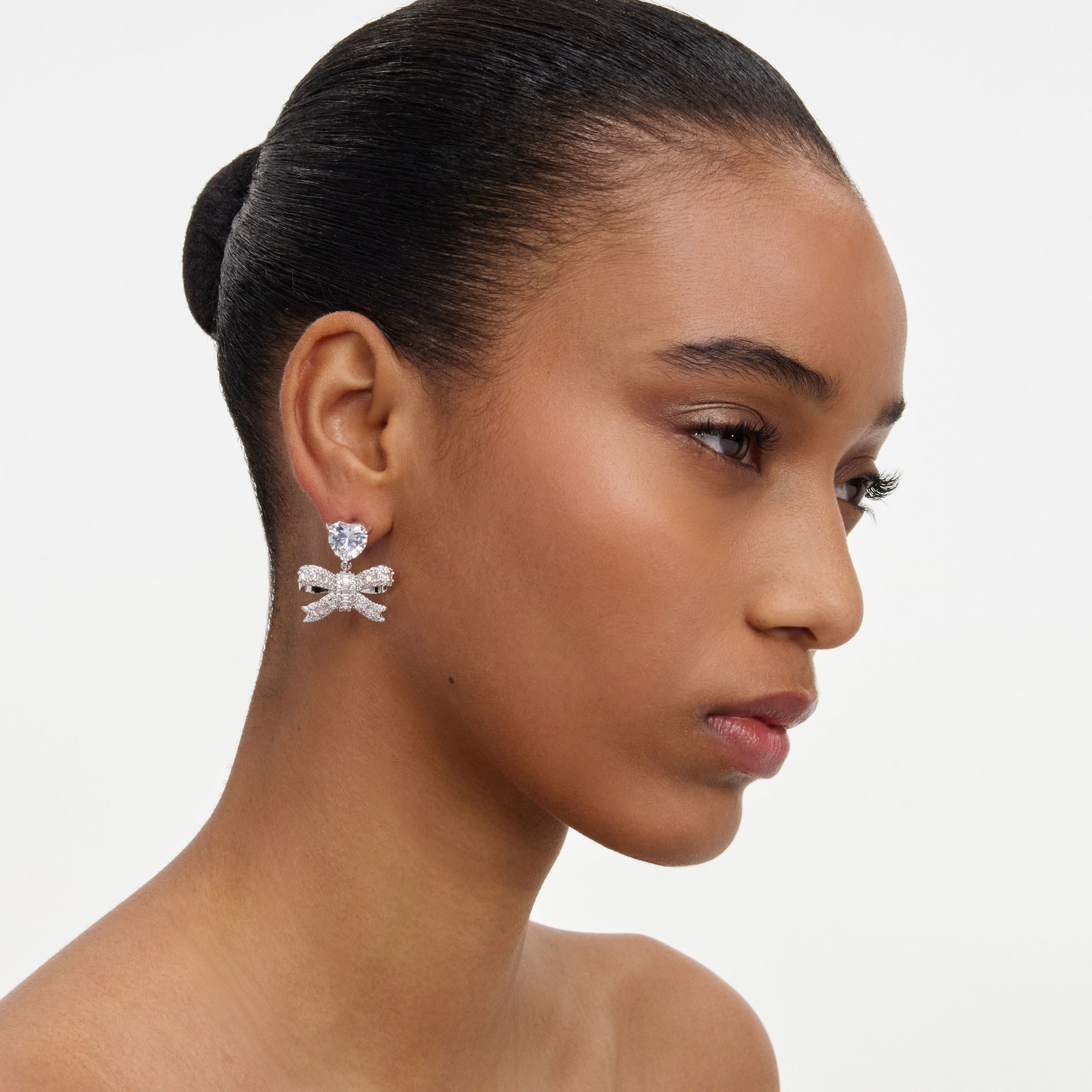 A close up of a woman wearing the Crystal Heart Bow Drop Earrings
