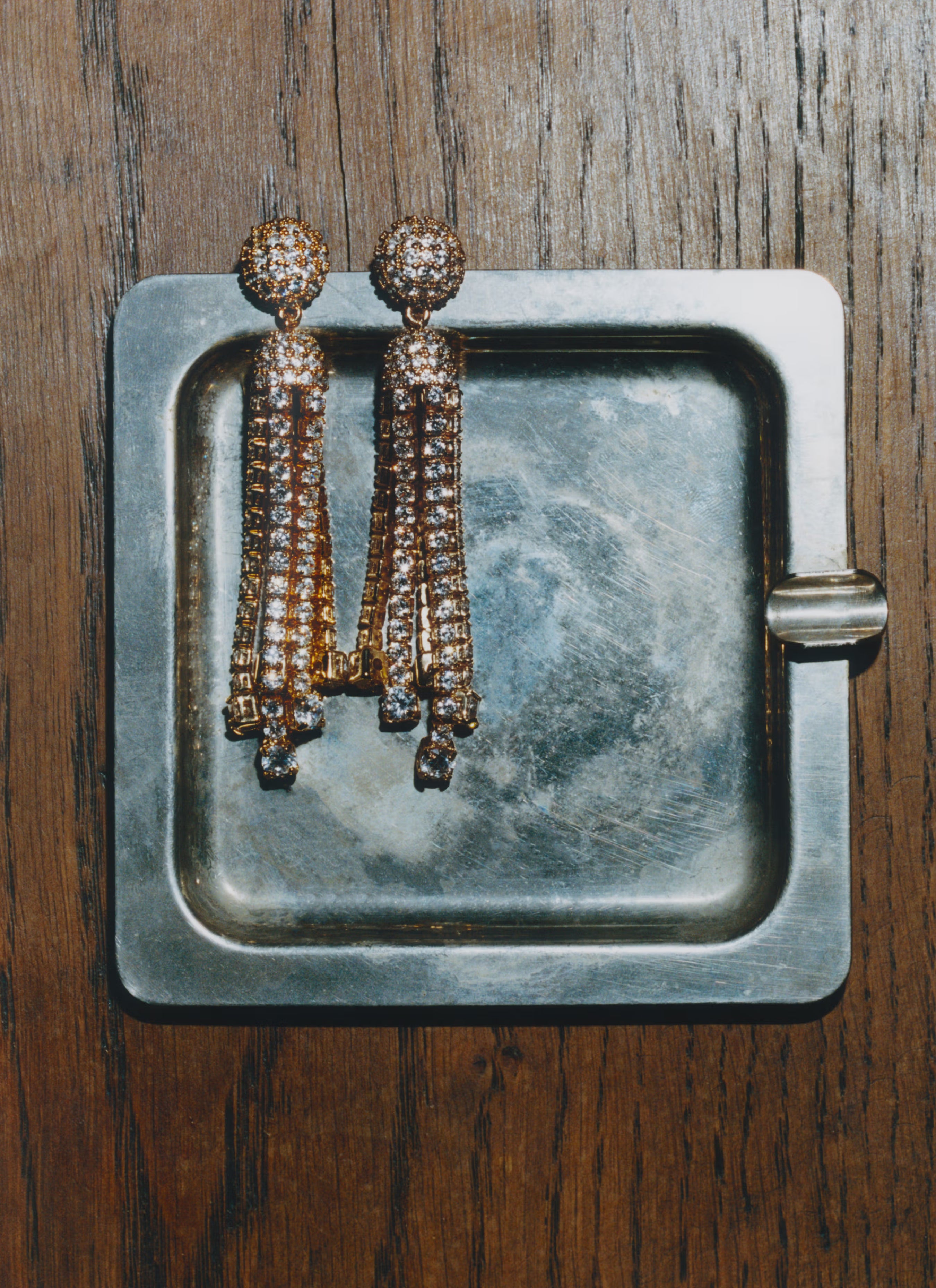 Pair of droplet earrings on a metallic tray with a wooden background.