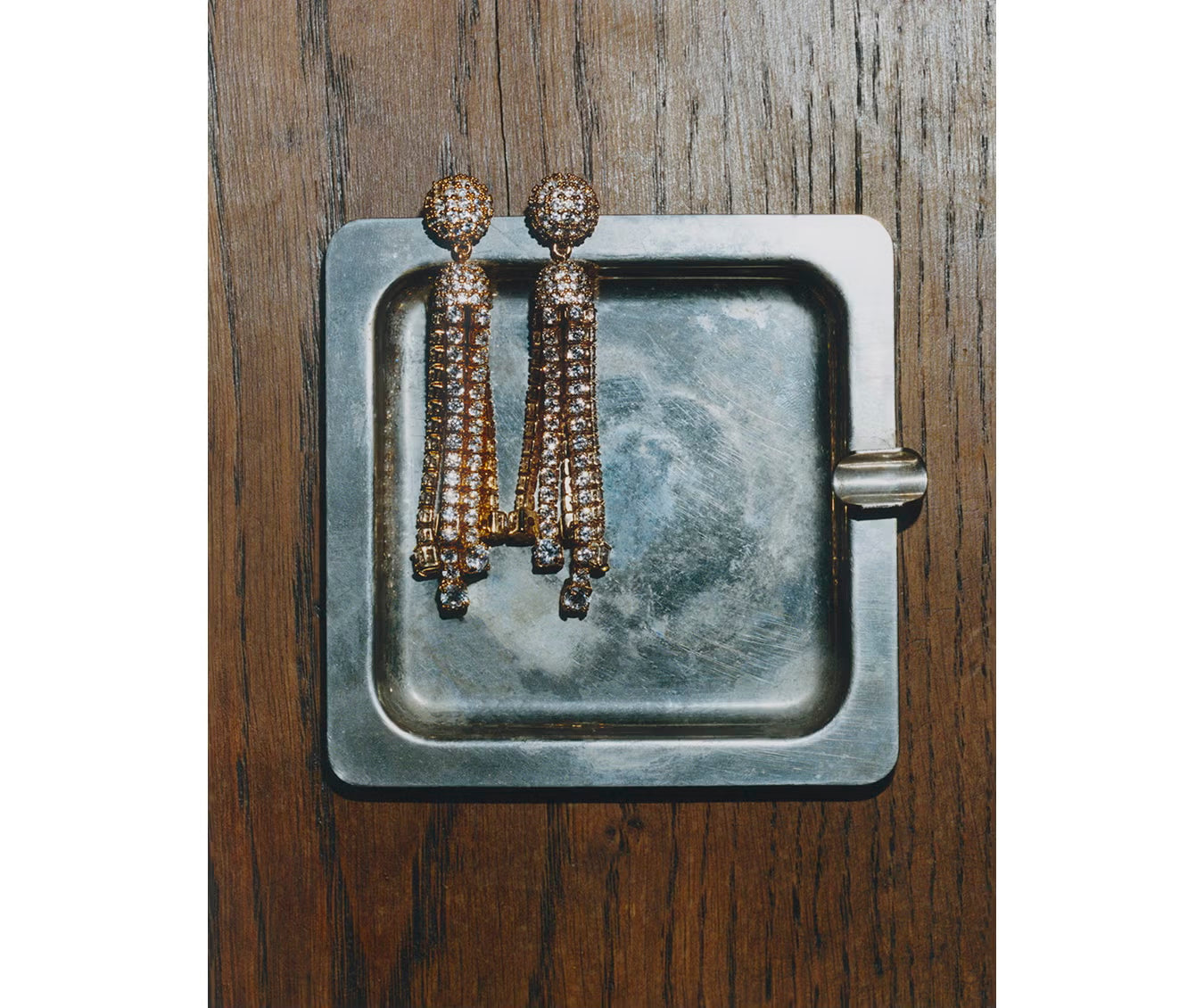 Pair of dangling earrings on a metallic surface with a wooden background.