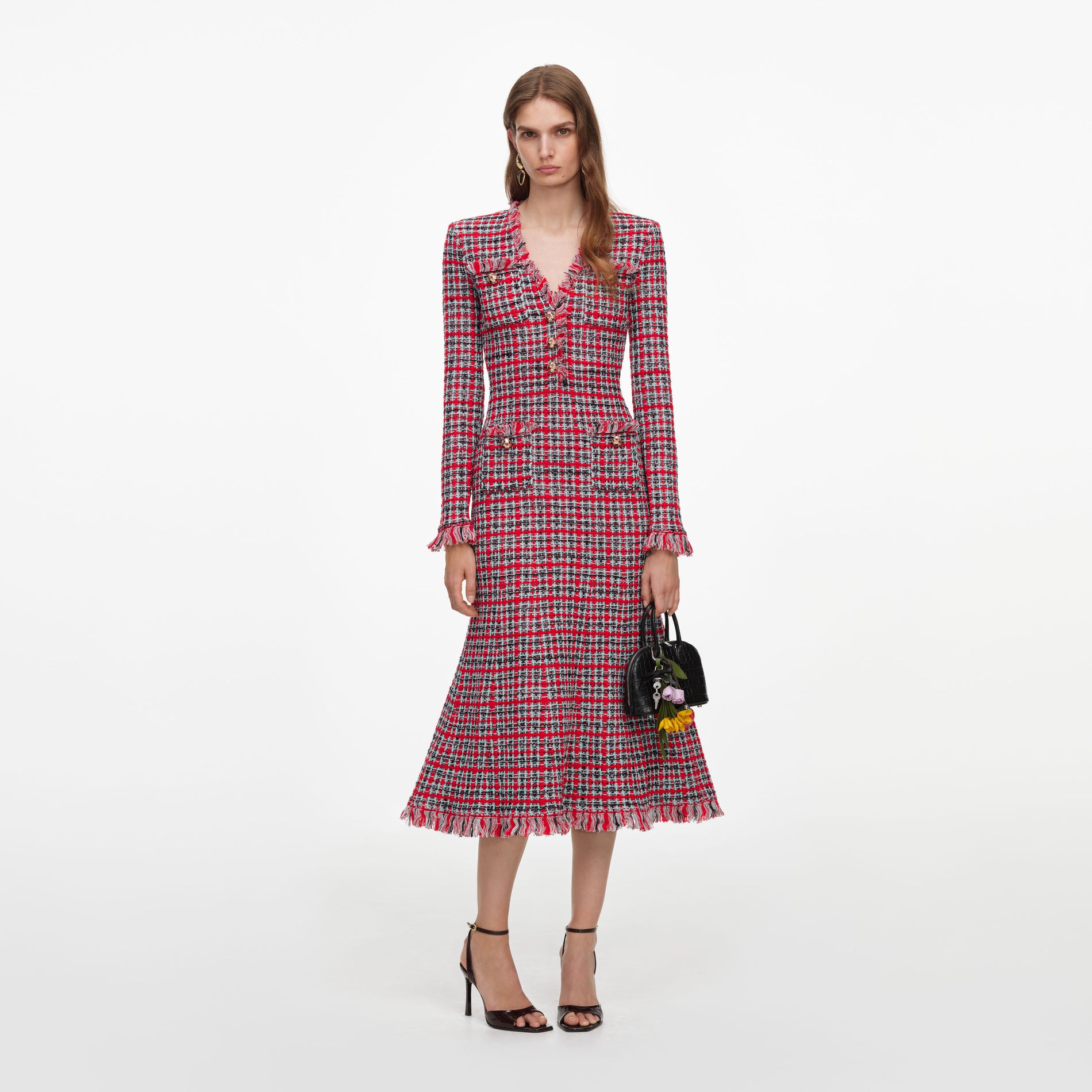 Woman in a red, black, and white plaid dress with fringe trim, holding a black handbag with flower charms