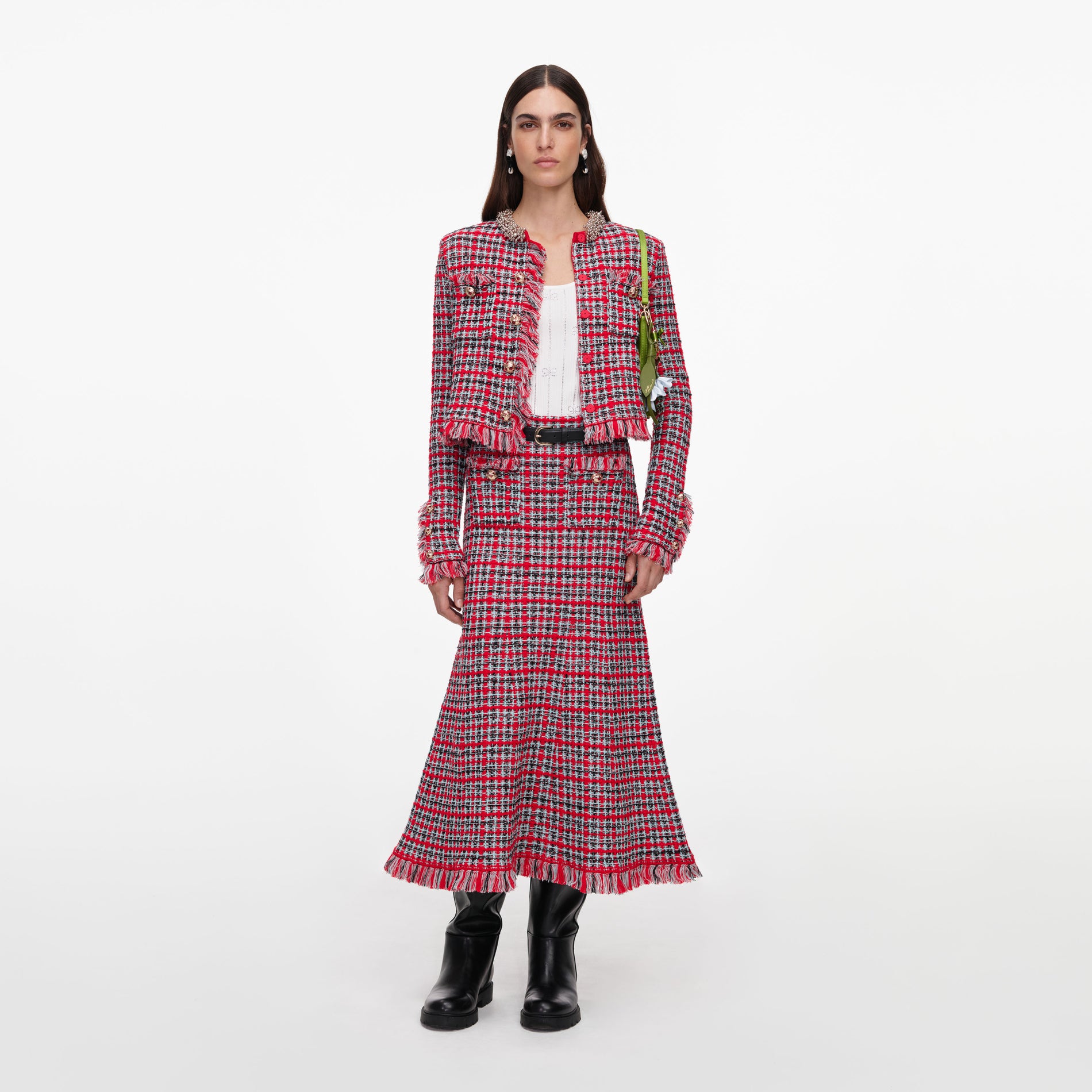 Woman in a red, black, and white plaid tweed jacket and matching midi skirt, with black boots and a green bag