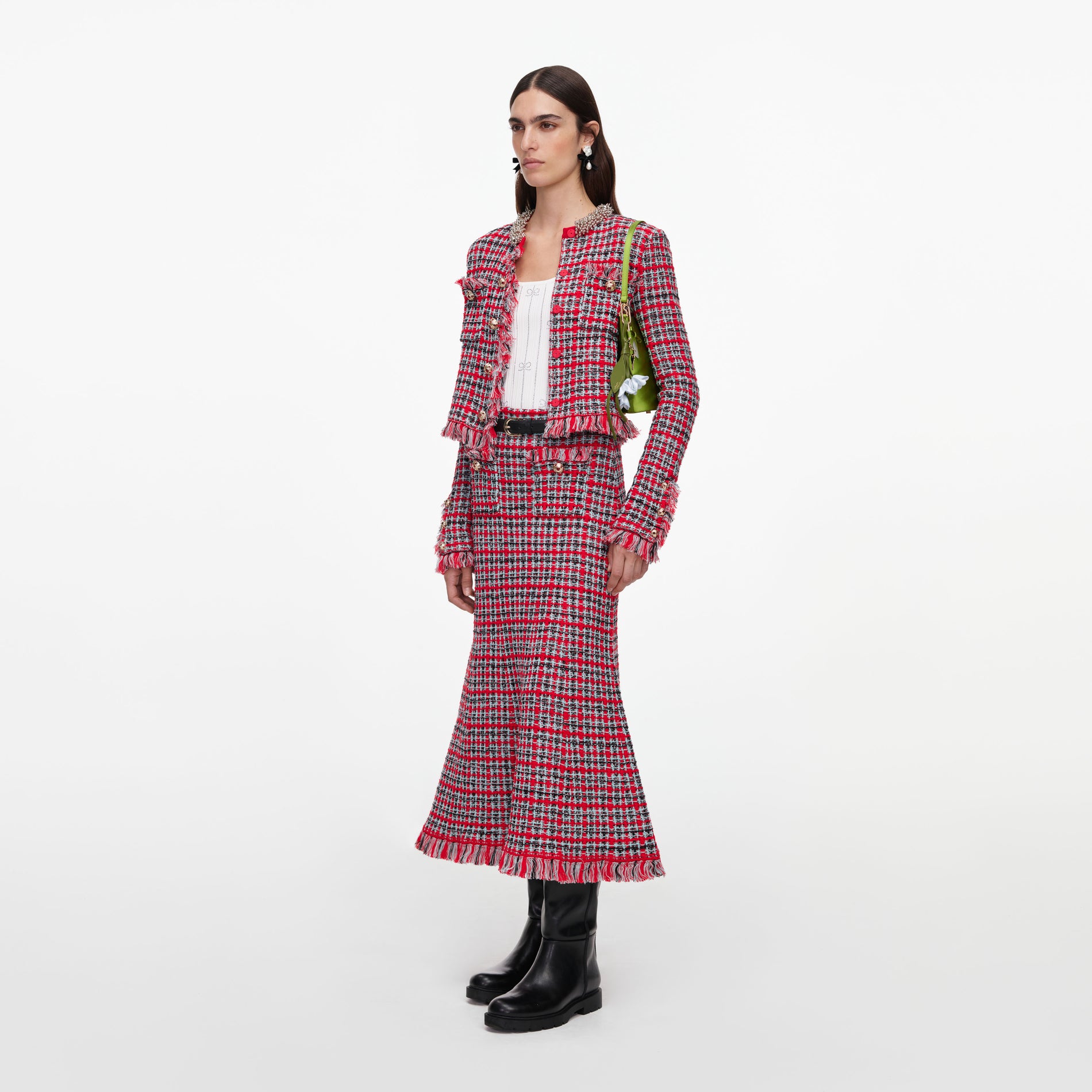 Woman in a red and black tweed jacket and matching skirt, with a white top, black boots, and a green handbag