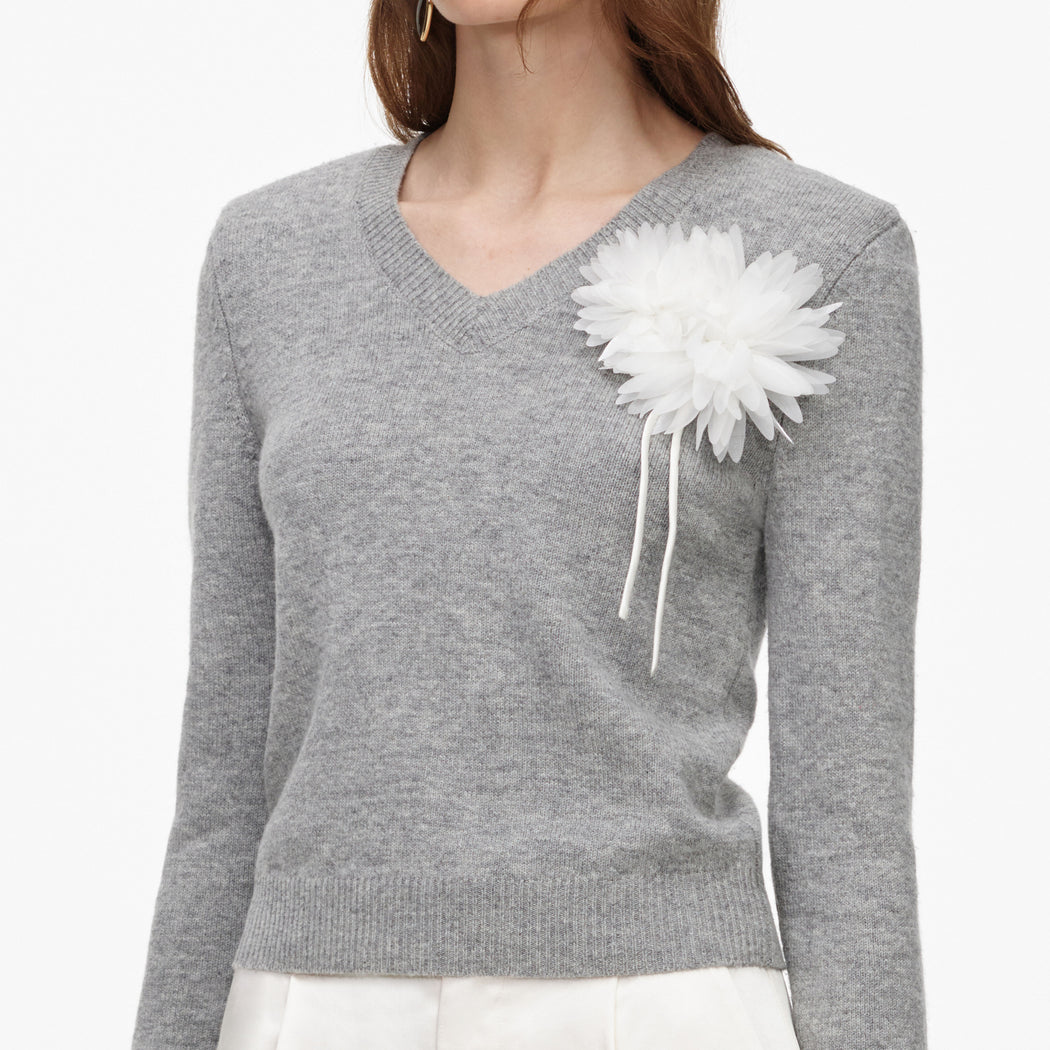 Woman wearing a grey v-neck sweater with a white floral brooch