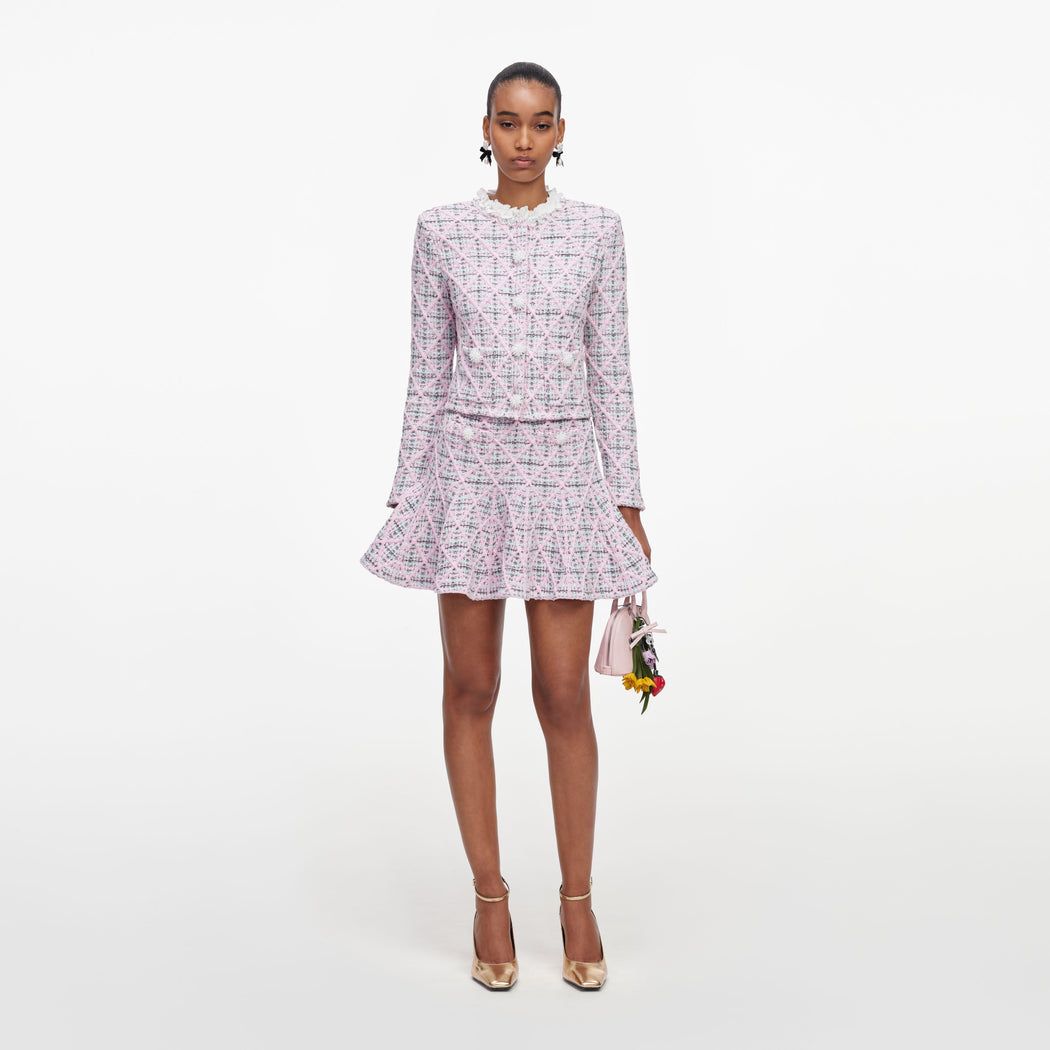 Woman in pink tweed jacket and matching skirt, holding a small pink handbag with flower charms