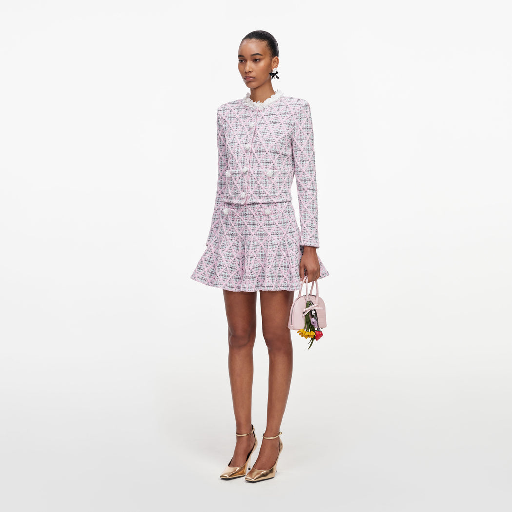 Model wearing a pink tweed jacket and matching skirt, gold heels, and a pink handbag with flower charms