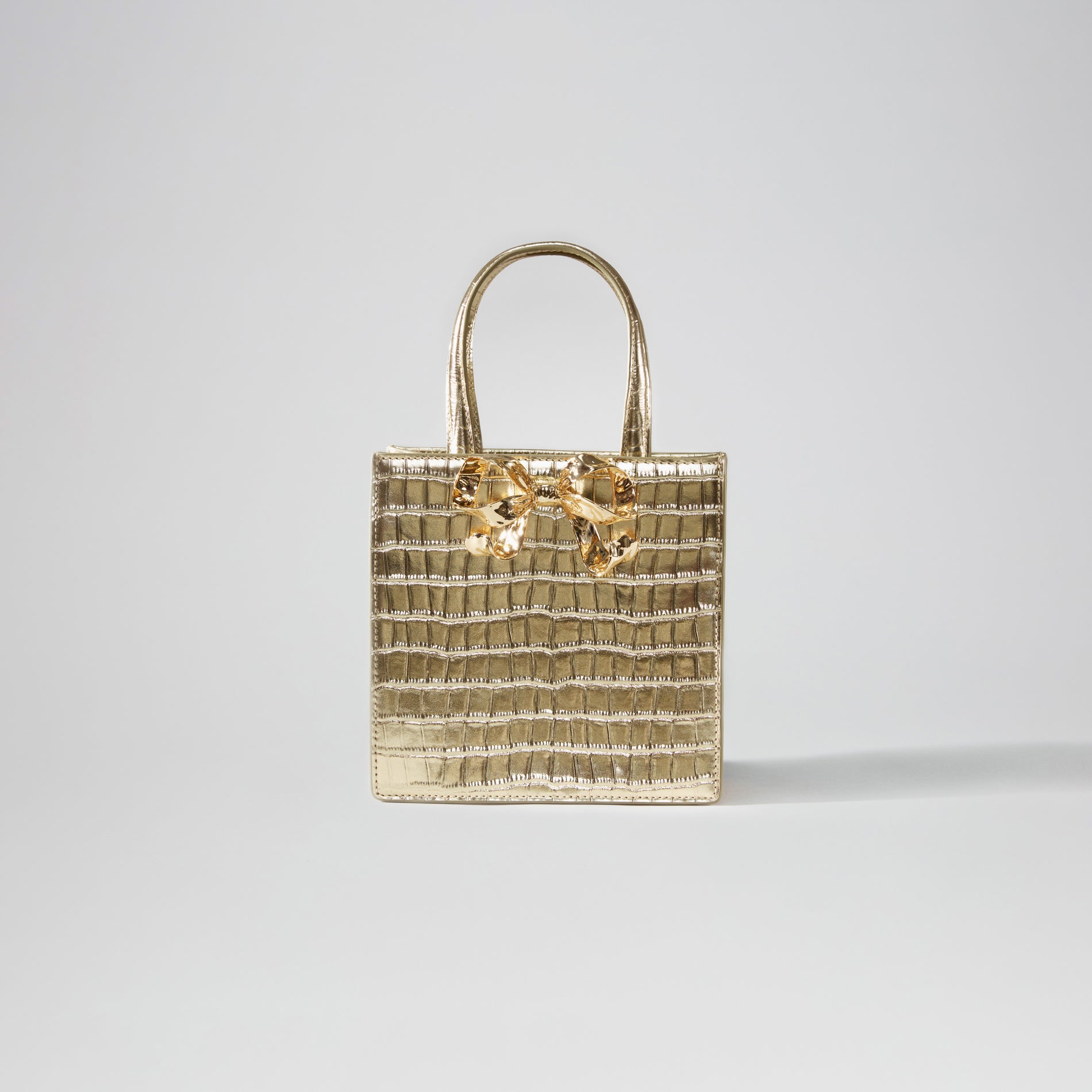 A woman wearing the Gold Croc Mini Tote Bow Bag