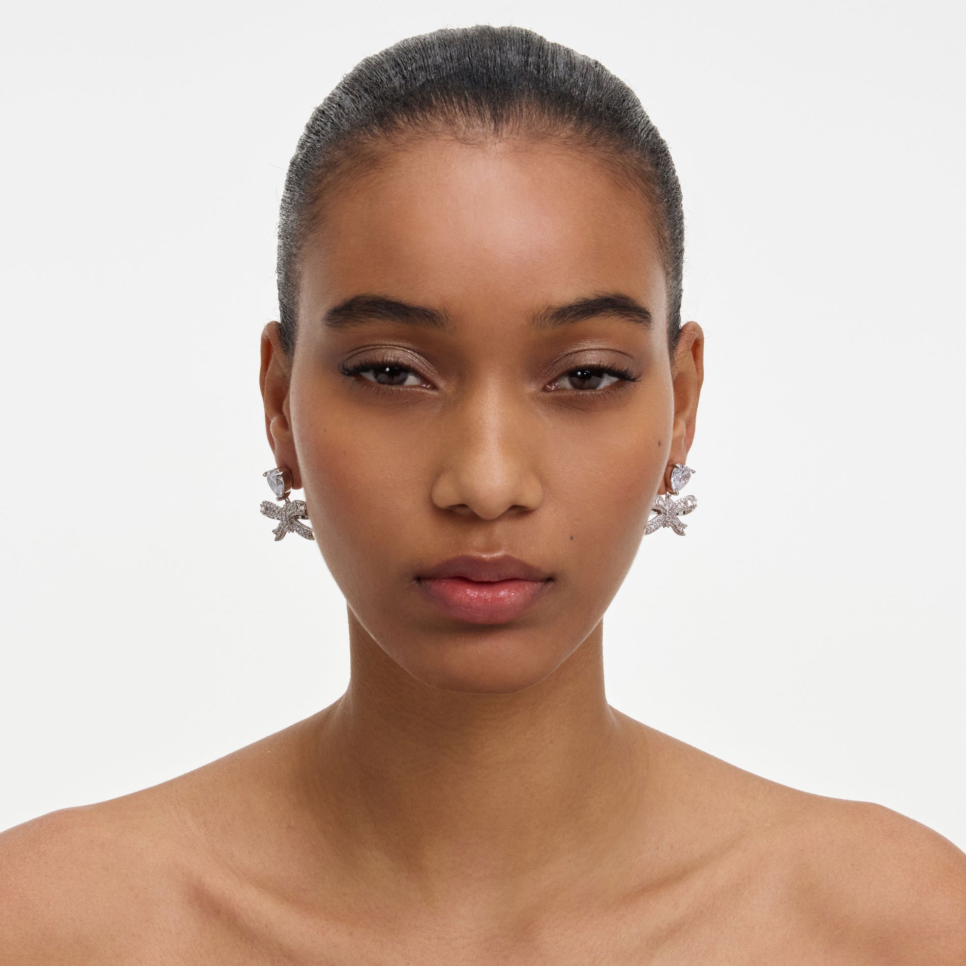A close up of a woman wearing the Crystal Heart Bow Drop Earrings