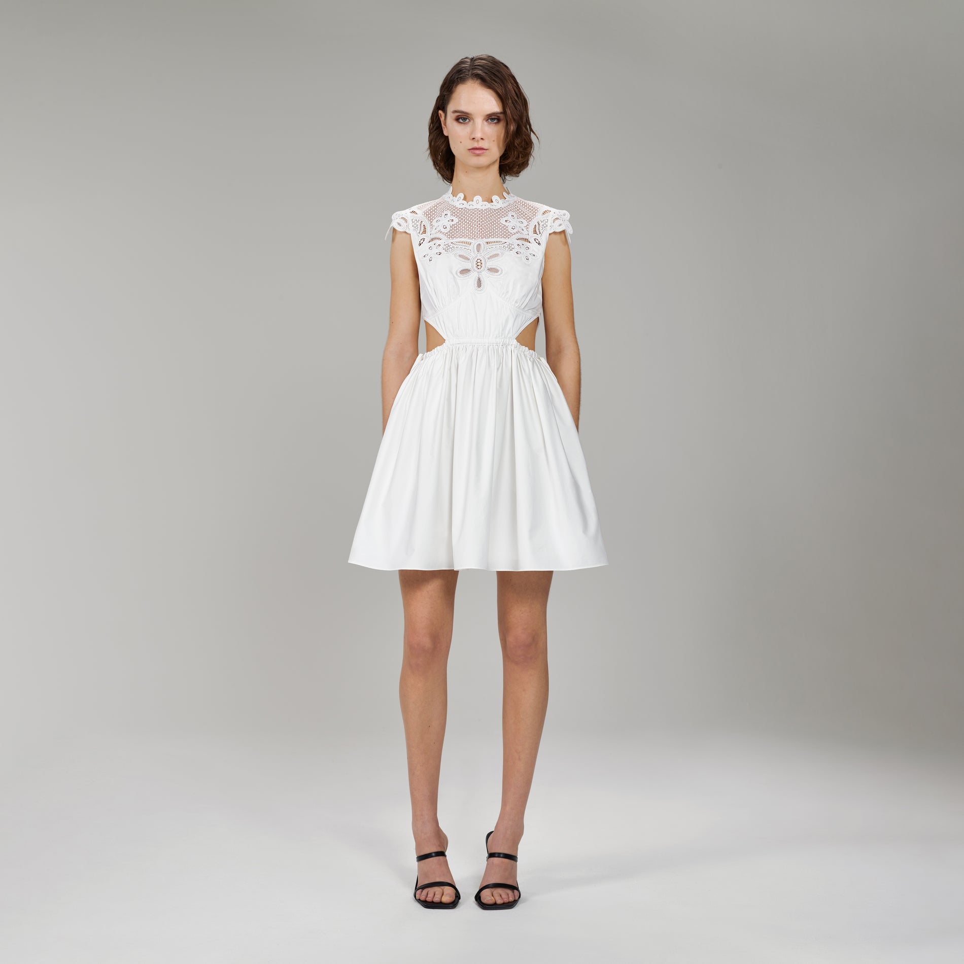 A woman wearing the White Cotton Guipure Lace Bib Mini Dress